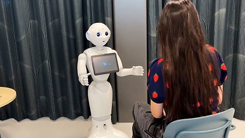 En robot med en skärm på magen pratar med en kvinna. 