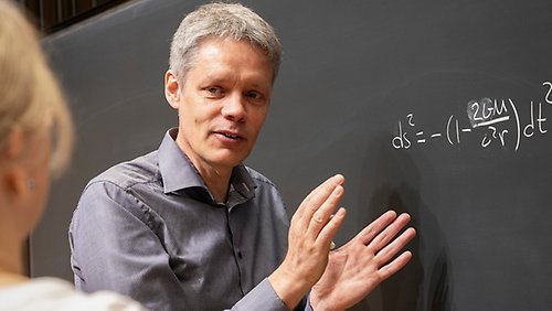 Ulf Danielsson står vid en svart tavla och förklarar en formel. 