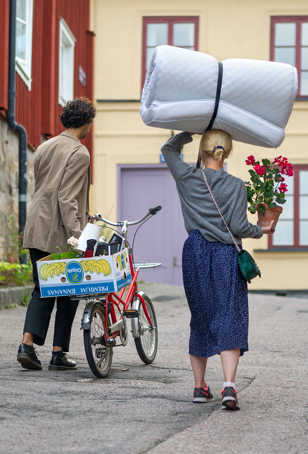 Students walking in Uppsala with boxes, a matress and a bike. 
