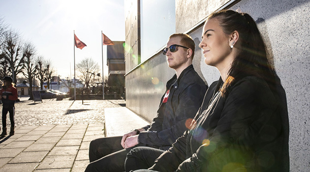 Två studenter på en bänk i solskenet utanför Uppsala universitets campusanläggning i Visby