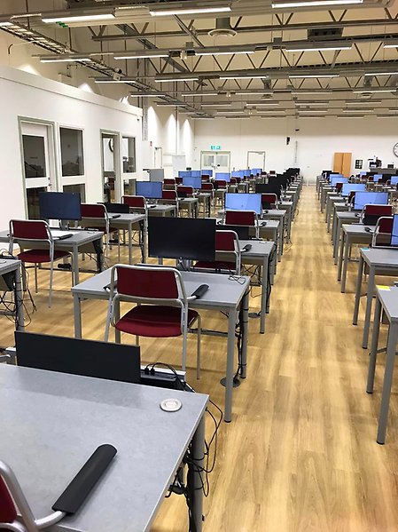 Hall with tables and chairs in rows. The tables also have a computer screen that can be lifted up and down
